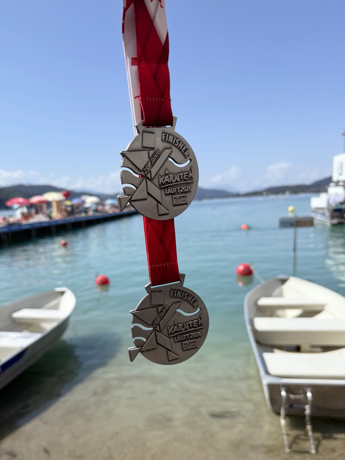 Zwei Finisher-Medaillen der Kärnten Läuft Bewerbe 2026 vor dem Wörthersee